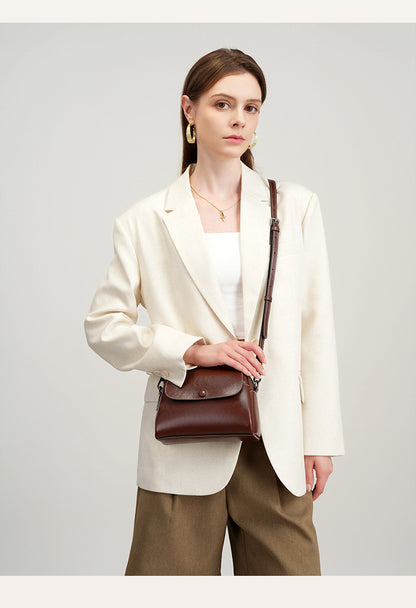 Model in cream blazer holding brown leather crossbody bag at waist