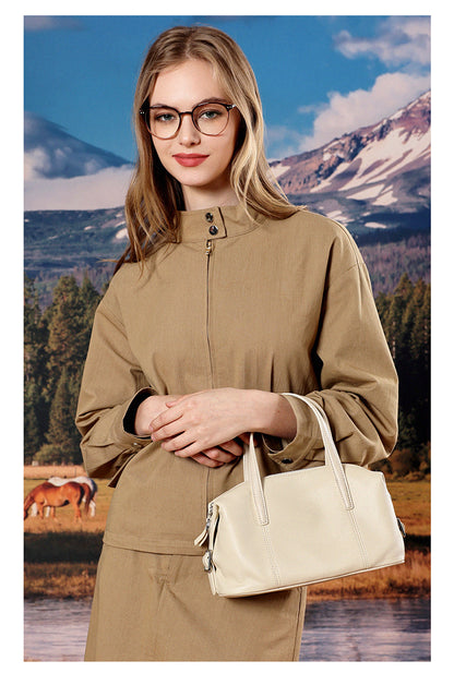 Model in beige jacket holding off-white bag near lake