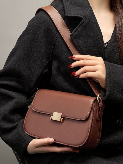 Model holding caramel leather shoulder bag at waist, three-quarter view