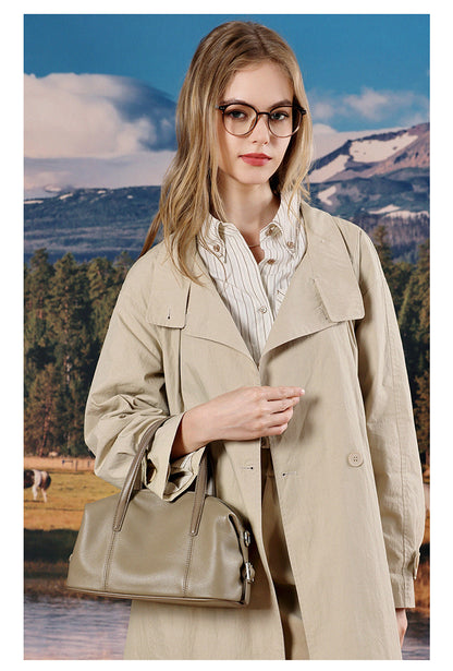 Model in beige outfit holding elephant gray bag near lake