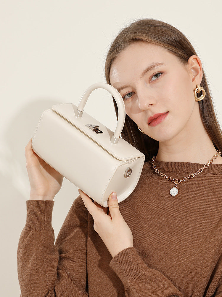 Model holding the cream box handbag by the top handle in a brown sweater