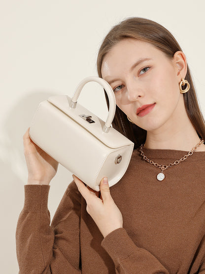 Model holding the cream box handbag by the top handle in a brown sweater