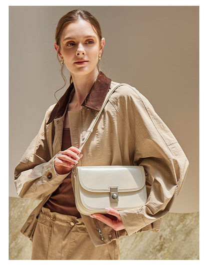 Model holding off-white leather messenger bag at waist height