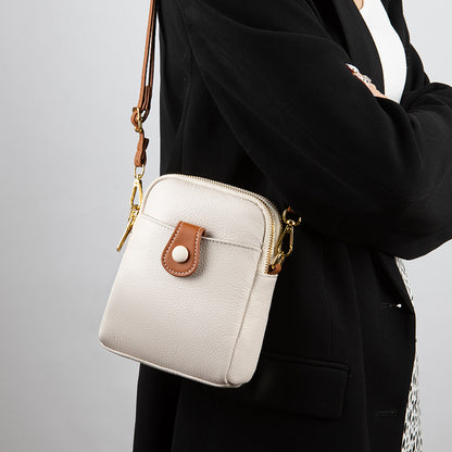 Off-white cowhide phone bag worn crossbody over a black coat showing strap detail