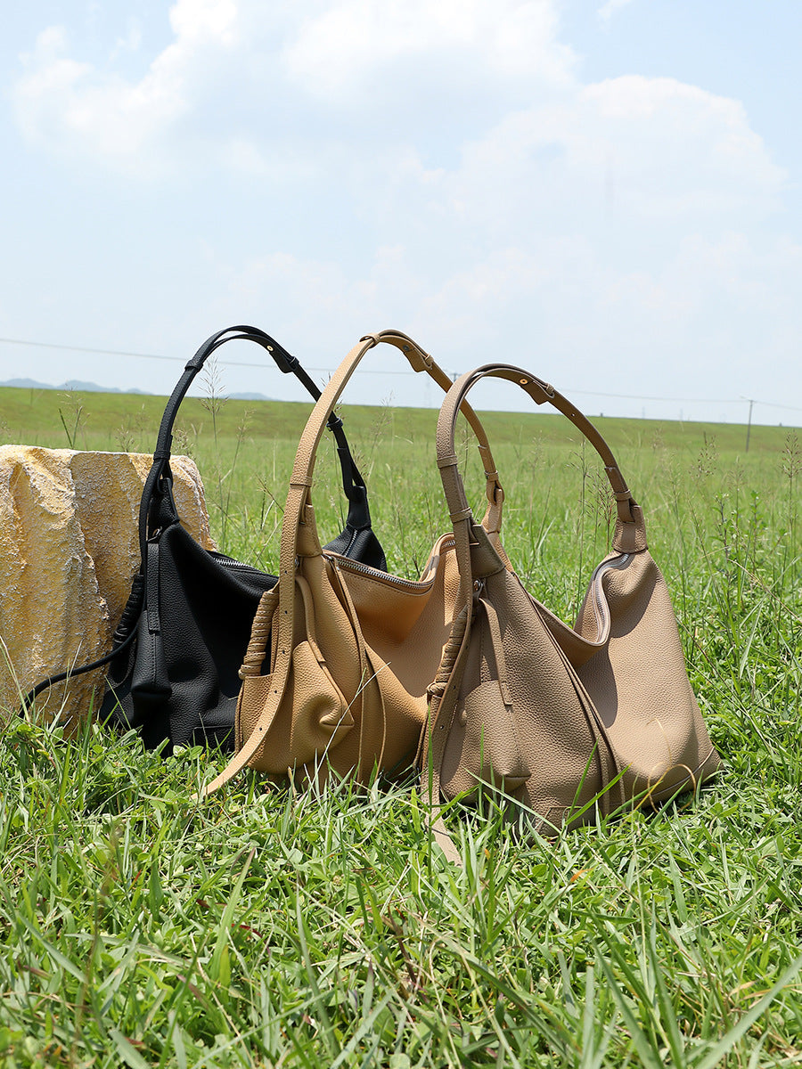 Three cowhide leather hobo bags in black, light brown, and taupe displayed on grass