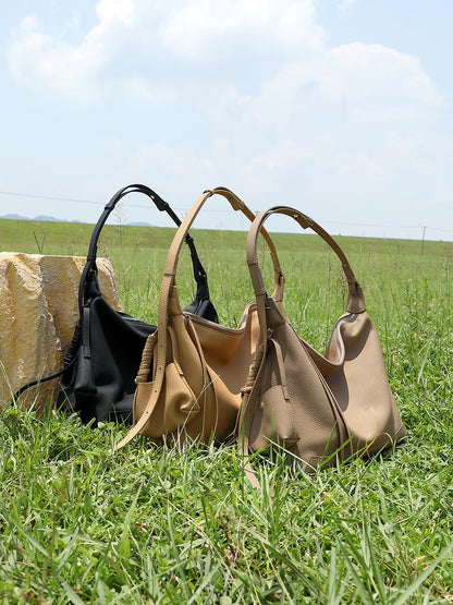 Three cowhide leather hobo bags in black, light brown, and taupe displayed on grass
