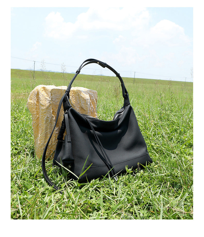 Black cowhide leather hobo bag with adjustable strap displayed on grass