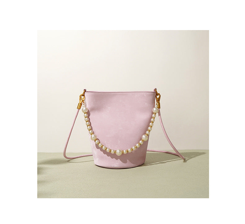Blush pink mini bucket bag with pearl chain on a green surface