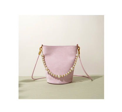 Blush pink mini bucket bag with pearl chain on a green surface