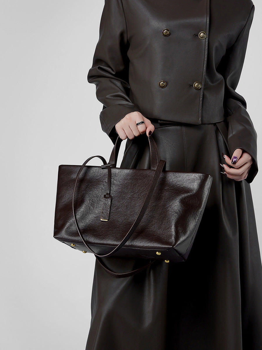Model in dark brown leather jacket holding brown leather tote bag