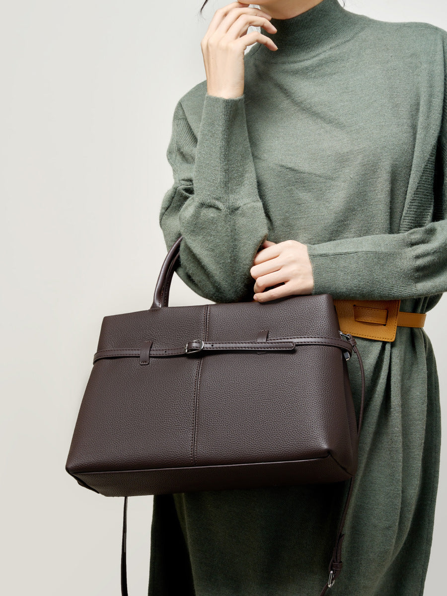 Model carrying coffee brown cowhide tote with green sweater and tan belt