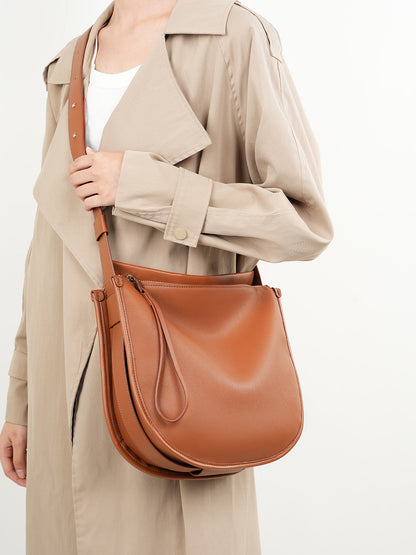 Tan leather hobo bag carried crossbody by model in beige trench