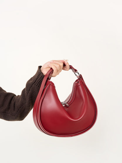 Hand holding burgundy leather crescent bag by the strap