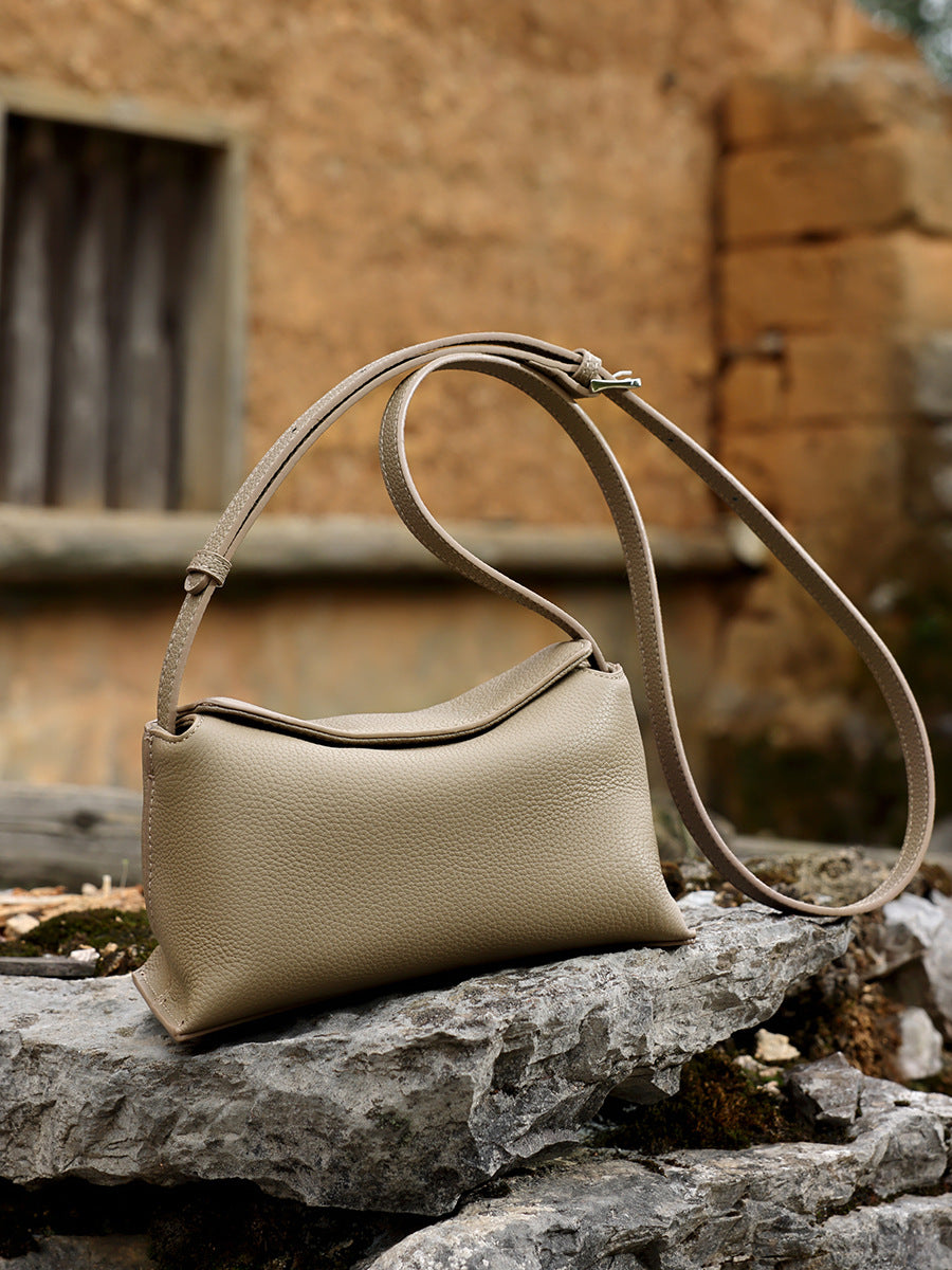 Khaki leather mini bag resting on a stone ledge with rustic wood backdrop