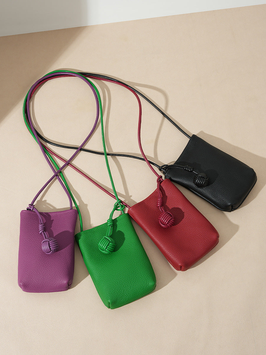 Flat lay of purple, green, red, and black pebbled leather mini bucket phone bags showing long straps