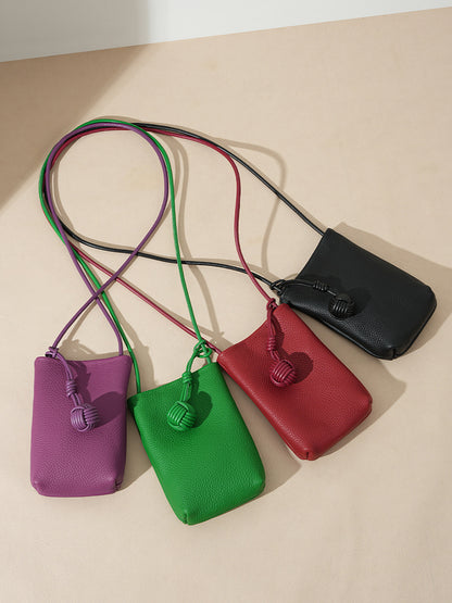 Flat lay of purple, green, red, and black pebbled leather mini bucket phone bags showing long straps