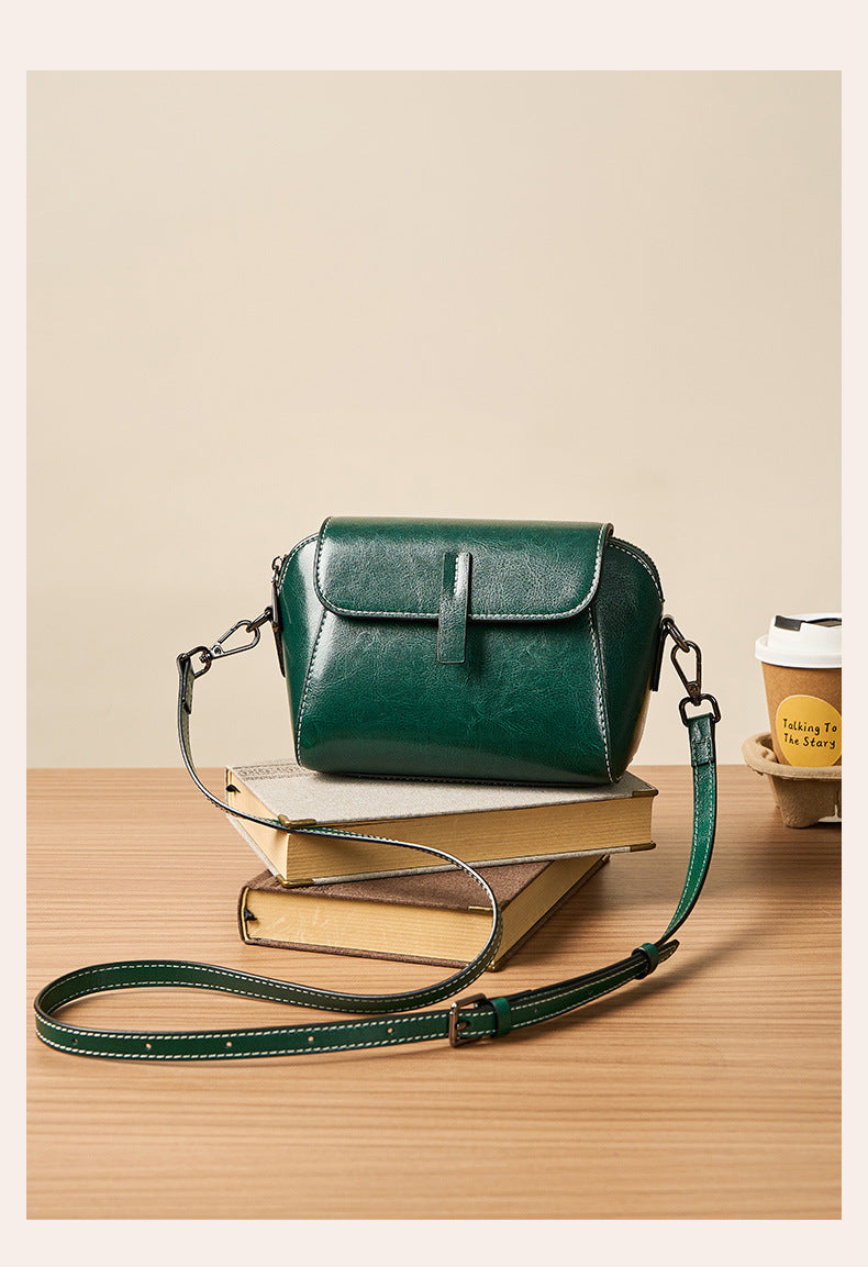 Deep green crossbody bag with adjustable strap beside coffee cup and books