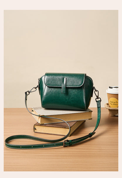 Deep green crossbody bag with adjustable strap beside coffee cup and books