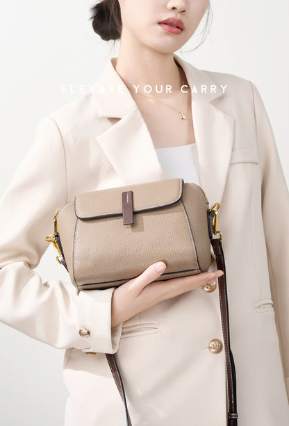Khaki shell crossbody bag held against a cream coat with gold-tone strap details