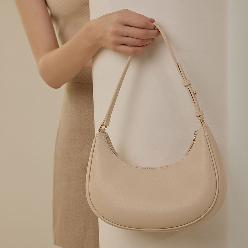 Cream crescent hobo bag hanging from hand showing adjustable buckle strap