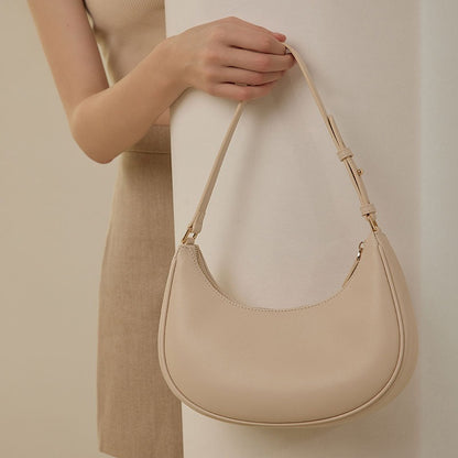 Cream crescent hobo bag hanging from hand showing adjustable buckle strap