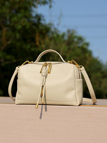 Off-white cowhide leather bag on outdoor ledge with greenery background
