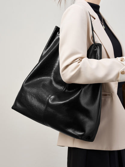 Black cowhide leather hobo tote bag carried under the arm with a beige blazer