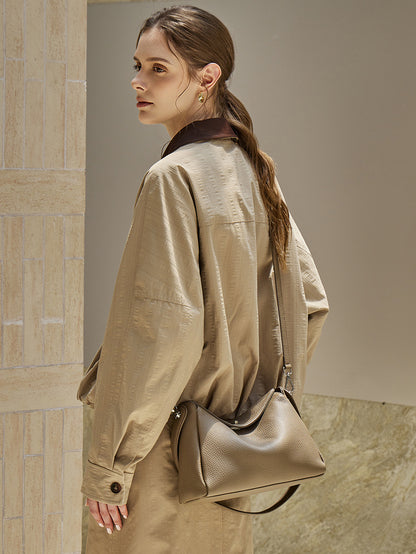 Three-quarter view of a model carrying a taupe pebbled leather shoulder bag in an urban setting