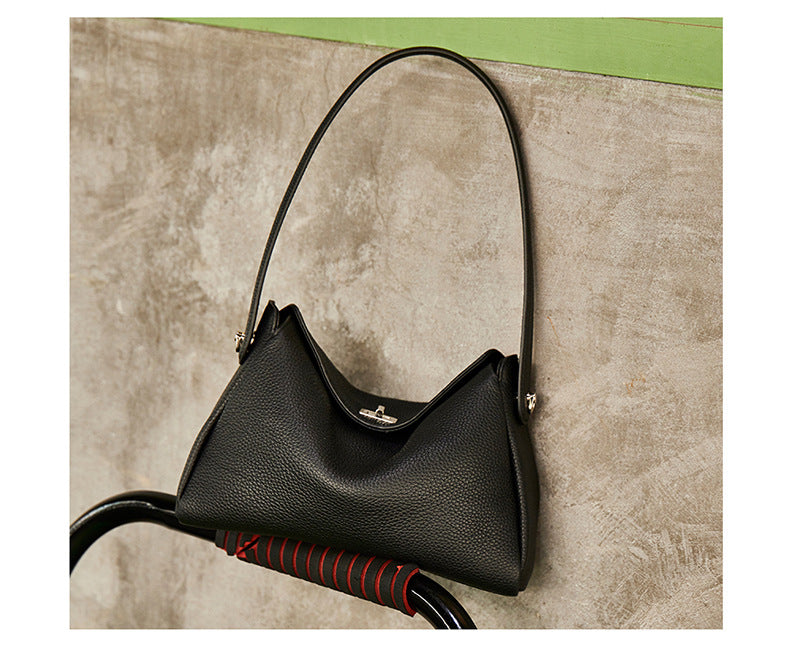 Black pebbled cowhide crossbody bag displayed against a concrete wall on a vintage bicycle frame