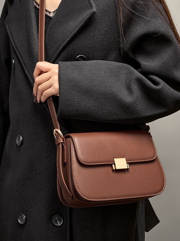 Close-up of caramel leather shoulder bag worn crossbody against black coat