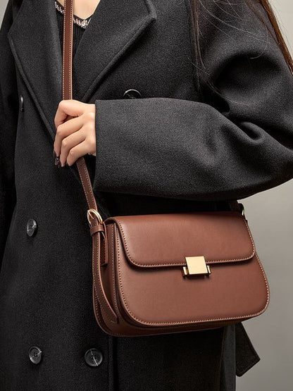Close-up of caramel leather shoulder bag worn crossbody against black coat
