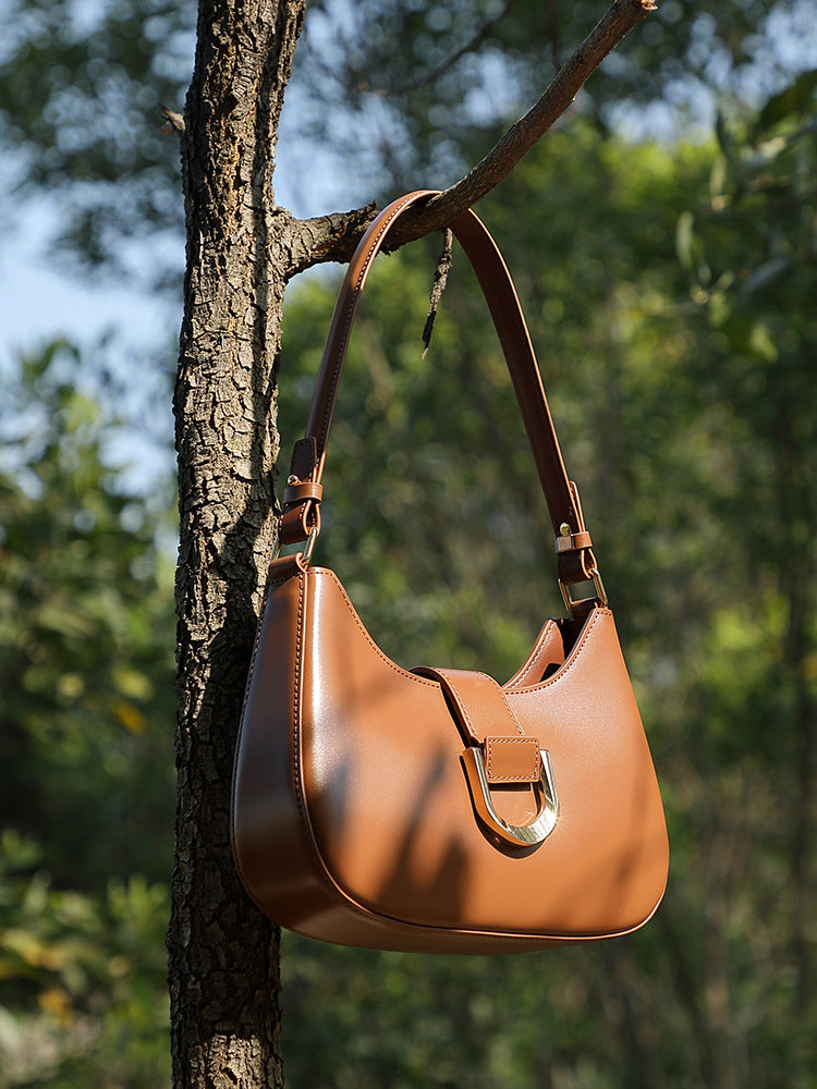 Caramel brown shoulder bag hanging on tree branch in nature