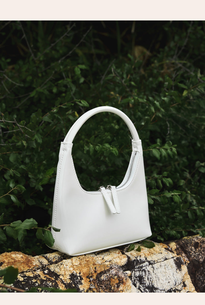 Cream patent mini hobo bag styled on rocks with greenery