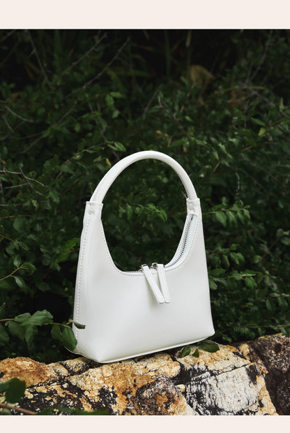 Cream patent mini hobo bag styled on rocks with greenery