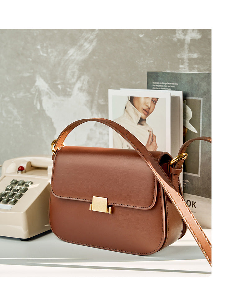 Caramel leather shoulder bag styled on a shelf beside a vintage telephone and magazine