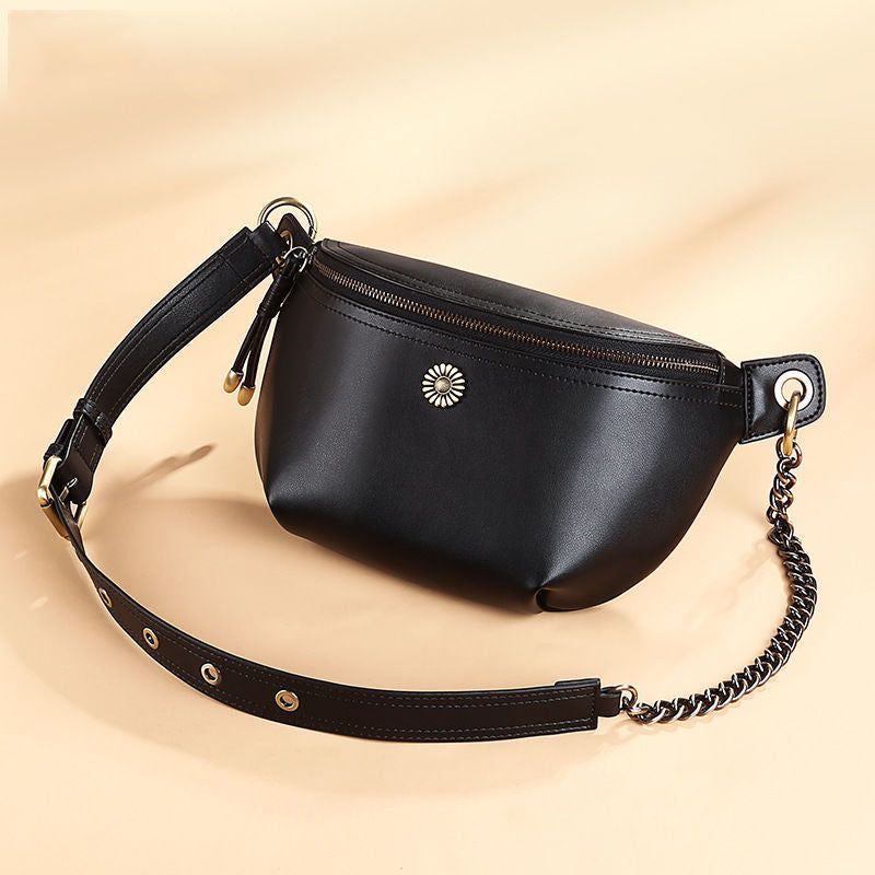 Black split leather belt bag with zip top and chain detail on a beige background
