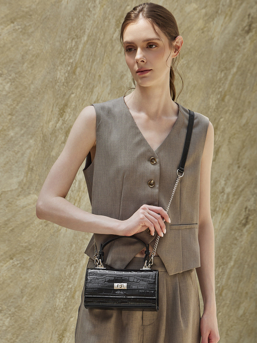 Model carrying black croco-embossed bag by the top handle at her side in a tailored outfit