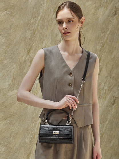 Model carrying black croco-embossed bag by the top handle at her side in a tailored outfit