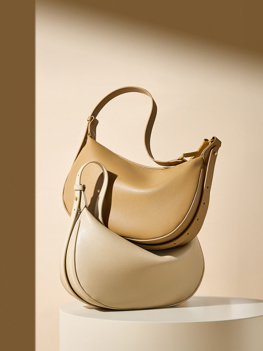 Stacked camel and off-white cowhide crescent underarm bags showing the curved silhouette