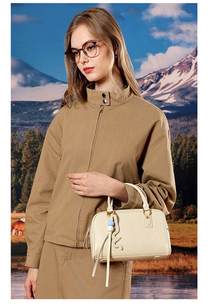 Model in tan outerwear holding a cream leather pillow bag by its top handles