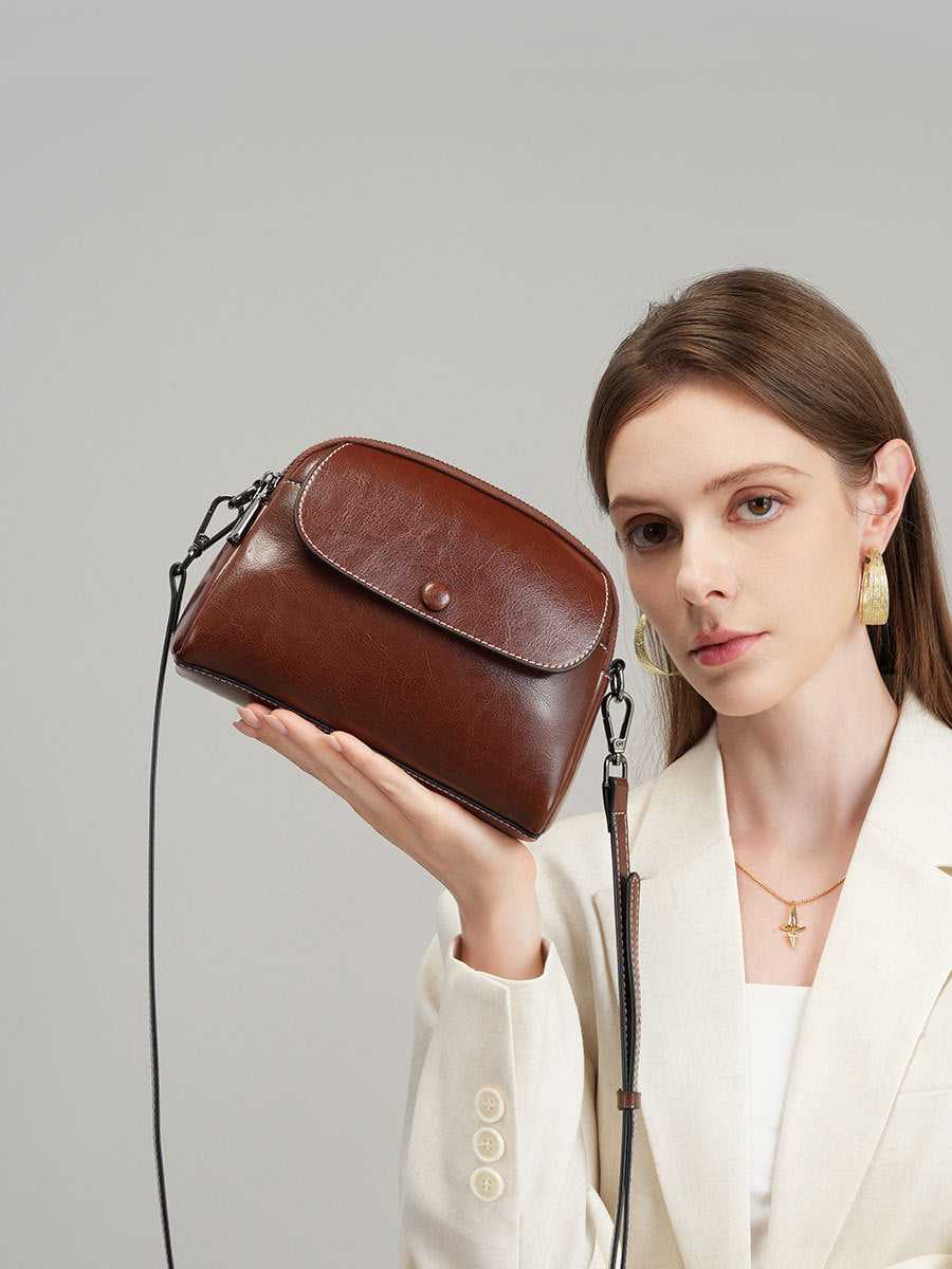 Model holding coffee leather crossbody bag at shoulder height