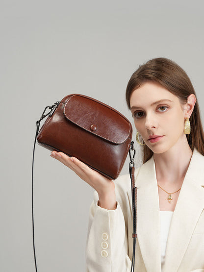 Model holding coffee leather crossbody bag at shoulder height