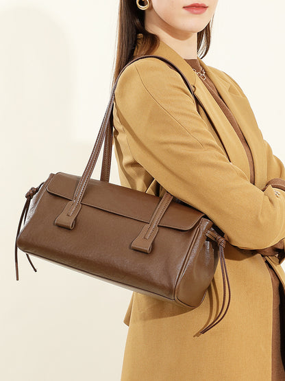 Brown cowhide leather shoulder bag worn under the arm by a model in tan coat