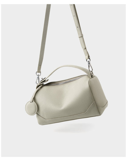 Ash white mini Boston bag suspended by adjustable strap on white background
