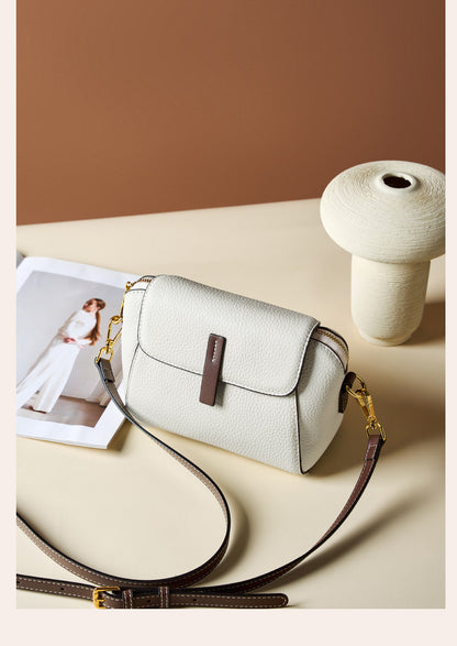 Ivory shell crossbody bag placed on a beige surface with detachable strap laid out