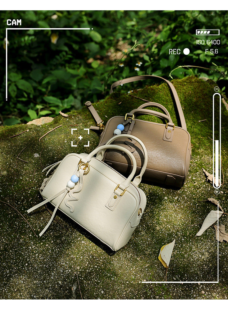 Two cowhide leather pillow bags in cream and taupe on a mossy rock with a camera frame overlay