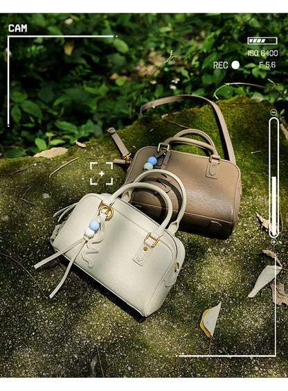 Two cowhide leather pillow bags in cream and taupe on a mossy rock with a camera frame overlay