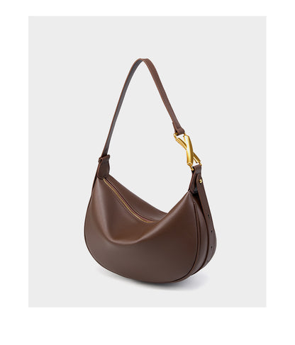 Coffee brown cowhide crescent underarm bag with gold-tone X buckle on a white background