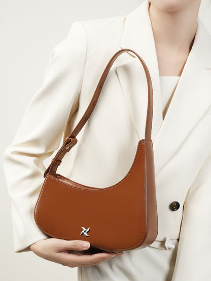 Brown leather crescent bag held by hand showing curved silhouette
