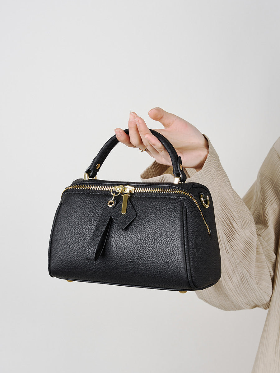 Model holding black mini Boston bag by the top handle in soft beige outfit